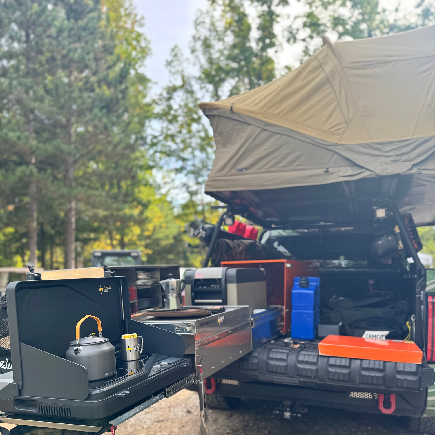 Camper truck with open cargo area and camping gear in a forest setting Lectric Boil on the Overland Kitchen pull out. The first portable induction stove and generator with a battery and dual burners for campers, outdoor workers, natural disasters — and anyone, anywhere, cooking or surviving off-grid.
#productimage
#overlander
#lifestyle